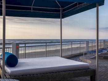 A tranquil beach view from a shaded cabana with loungers and a calm sea