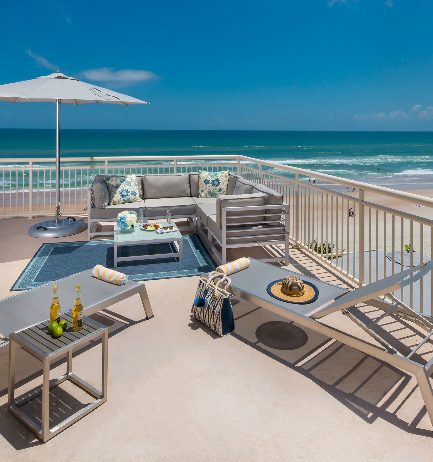 Oceanfront balcony with furniture, sun umbrella, and beach view.