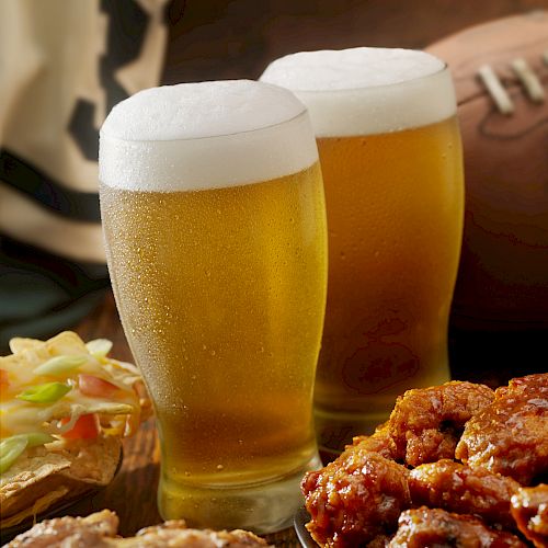 Two glasses of beer, wings, celery, and a football in the background.